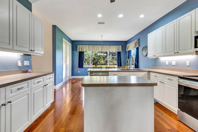 kitchen with pendant lighting, sink, stainless steel appliances, white cabinets, and a kitchen island