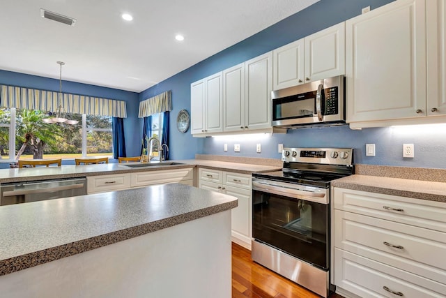 kitchen featuring appliances with stainless steel finishes, decorative light fixtures, sink, white cabinets, and light wood-type flooring