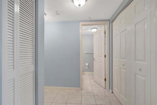 hall featuring a textured ceiling, light tile patterned flooring, and baseboards