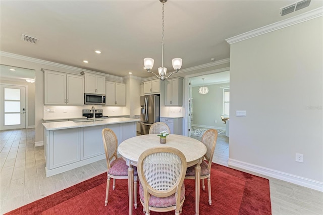 dining space featuring ornamental molding, sink, a notable chandelier, and light hardwood / wood-style flooring