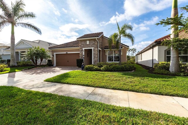 mediterranean / spanish-style house featuring a garage, a tile roof, stone siding, decorative driveway, and a front lawn