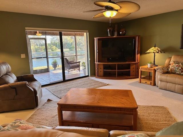 carpeted living area with a textured ceiling and ceiling fan