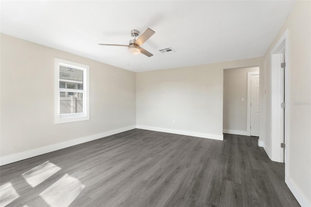 spare room featuring baseboards, visible vents, a ceiling fan, and dark wood finished floors