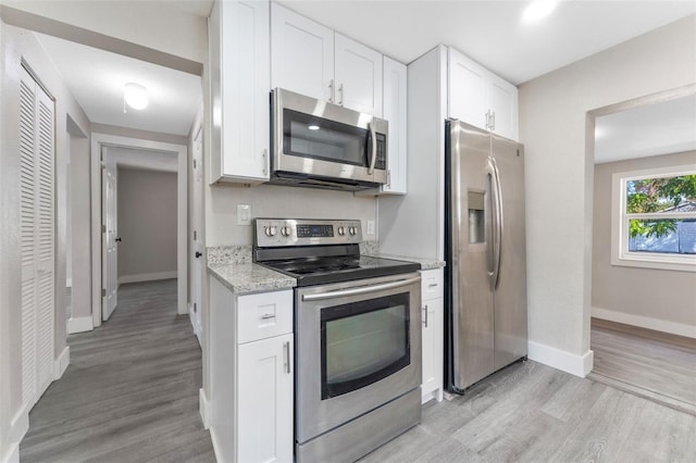 kitchen featuring light stone counters, stainless steel appliances, white cabinets, and light wood-style flooring
