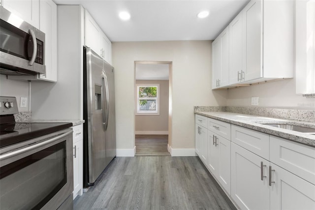 kitchen with light stone counters, stainless steel appliances, white cabinetry, and wood finished floors