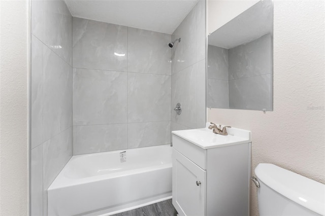 bathroom with wood finished floors, vanity, toilet, a textured wall, and shower / tub combination