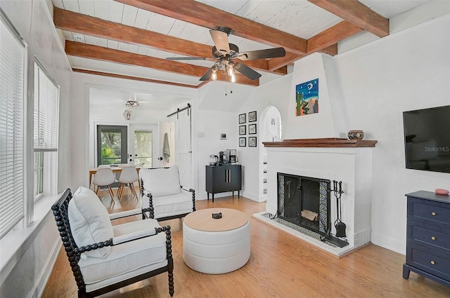 living room with lofted ceiling with beams, a large fireplace, ceiling fan, light hardwood / wood-style floors, and a barn door