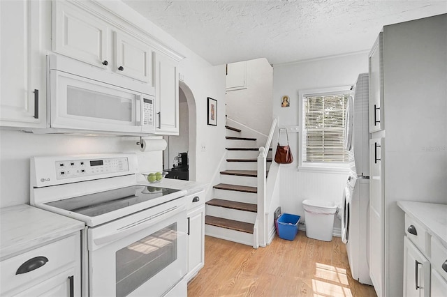 kitchen with white cabinetry, white appliances, light hardwood / wood-style flooring, and a textured ceiling