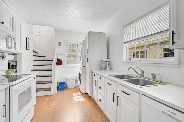 kitchen with stacked washer and dryer, white cabinetry, sink, and white appliances