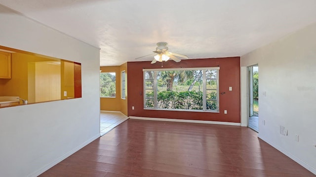 empty room with plenty of natural light, dark wood-type flooring, and ceiling fan