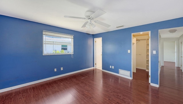 unfurnished bedroom featuring a walk in closet, dark wood-type flooring, ceiling fan, and a closet