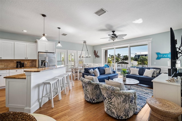 living room with a textured ceiling, ceiling fan with notable chandelier, a wealth of natural light, and light hardwood / wood-style flooring