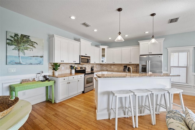 kitchen featuring a center island with sink, stainless steel appliances, light stone counters, pendant lighting, and white cabinetry