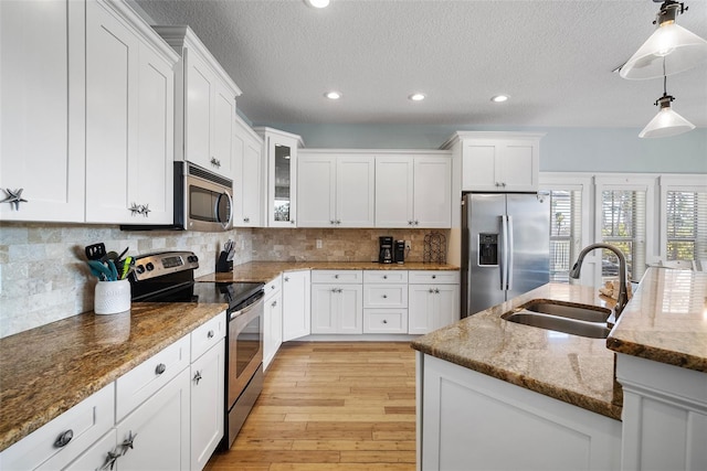 kitchen featuring appliances with stainless steel finishes, sink, white cabinetry, pendant lighting, and light stone countertops