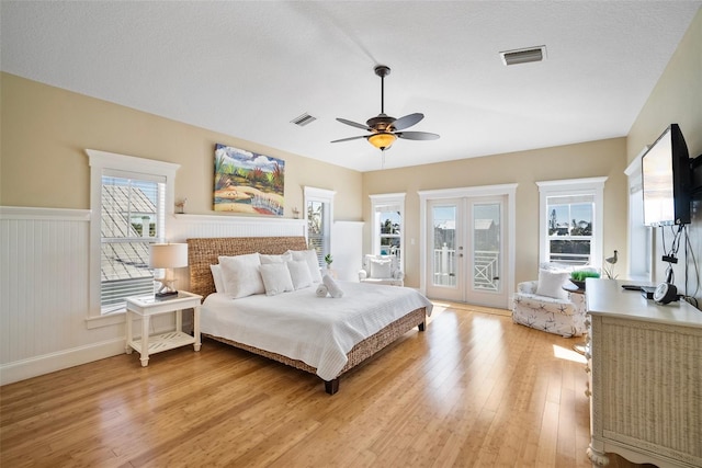 bedroom featuring light hardwood / wood-style flooring, a textured ceiling, ceiling fan, french doors, and access to exterior