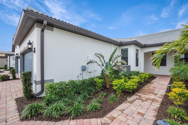 view of home's exterior featuring an attached garage, a tiled roof, and stucco siding