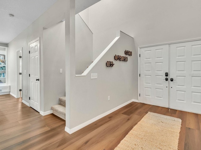 entryway featuring wood finished floors, baseboards, and stairs