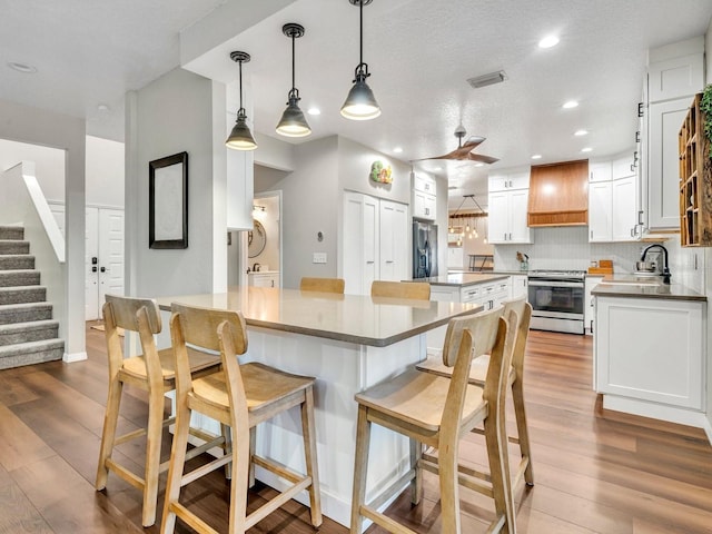 kitchen featuring stainless steel appliances, a kitchen island, white cabinets, hanging light fixtures, and custom range hood