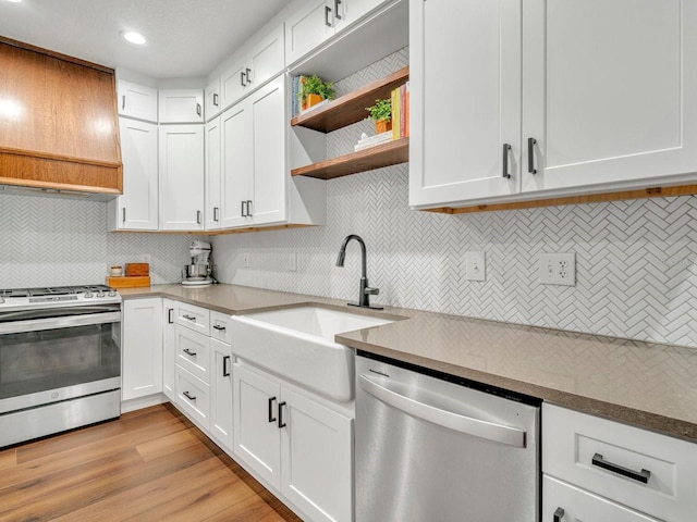 kitchen with white cabinets, custom exhaust hood, stainless steel appliances, light wood-style floors, and a sink