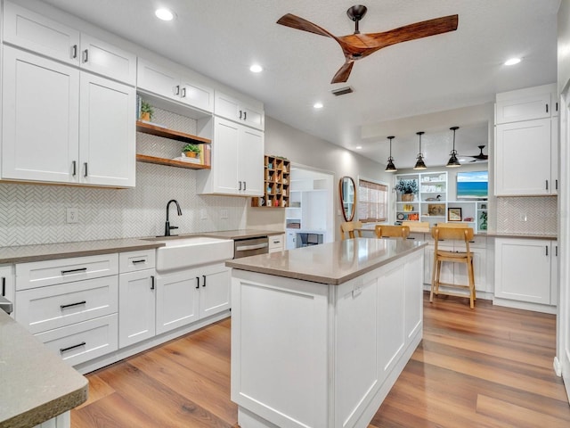 kitchen featuring a center island, light countertops, white cabinetry, a sink, and ceiling fan