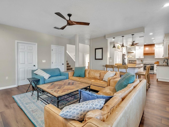 living area with light wood-type flooring, ceiling fan, stairway, and recessed lighting