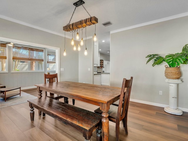 dining room featuring ornamental molding, light wood-type flooring, visible vents, and baseboards