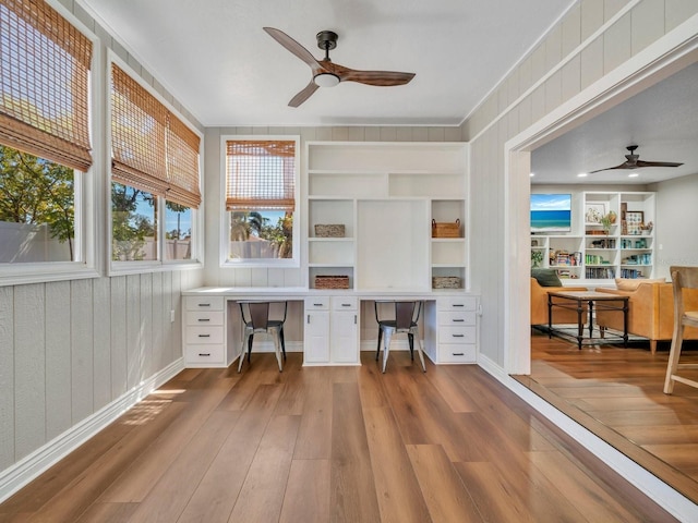 office space featuring ceiling fan, wood finished floors, built in study area, and built in shelves