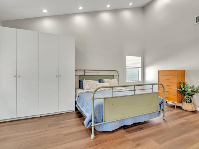 bedroom with visible vents, a towering ceiling, and light wood-style flooring