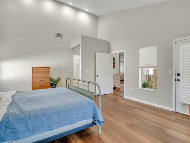 bedroom with recessed lighting, a high ceiling, wood finished floors, visible vents, and baseboards