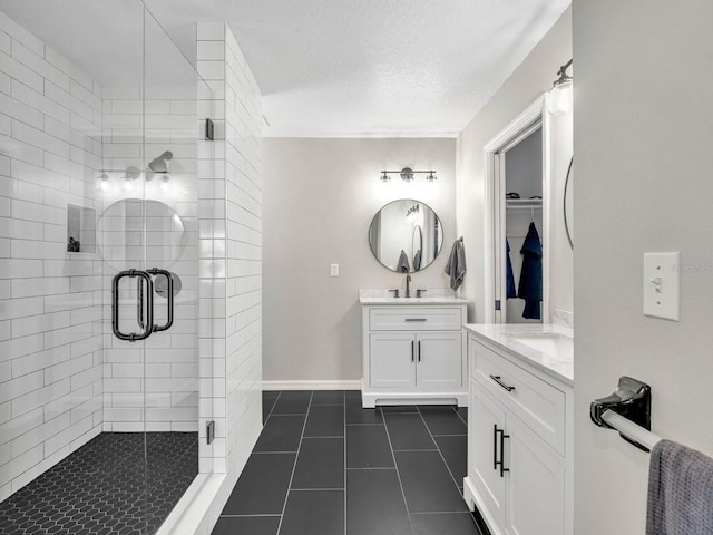 bathroom featuring two vanities, a spacious closet, a stall shower, a textured ceiling, and tile patterned flooring