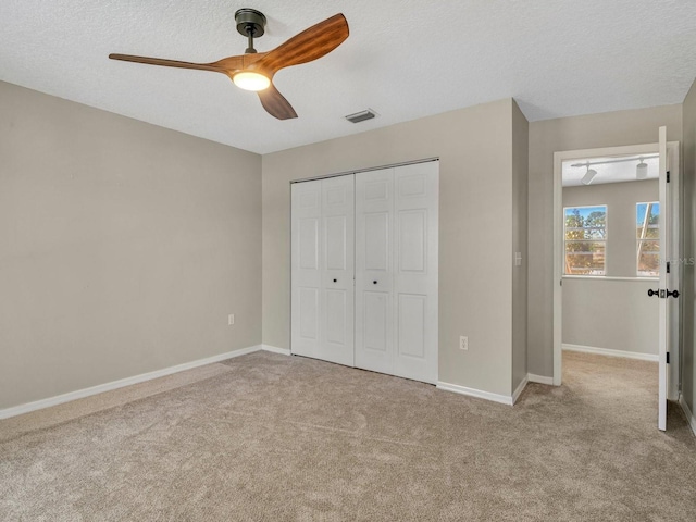 unfurnished bedroom featuring a textured ceiling, light colored carpet, visible vents, baseboards, and a closet