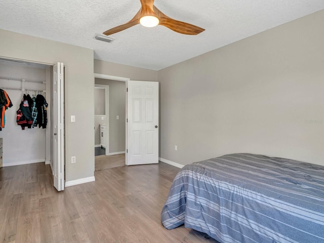 bedroom with a walk in closet, a textured ceiling, baseboards, and wood finished floors