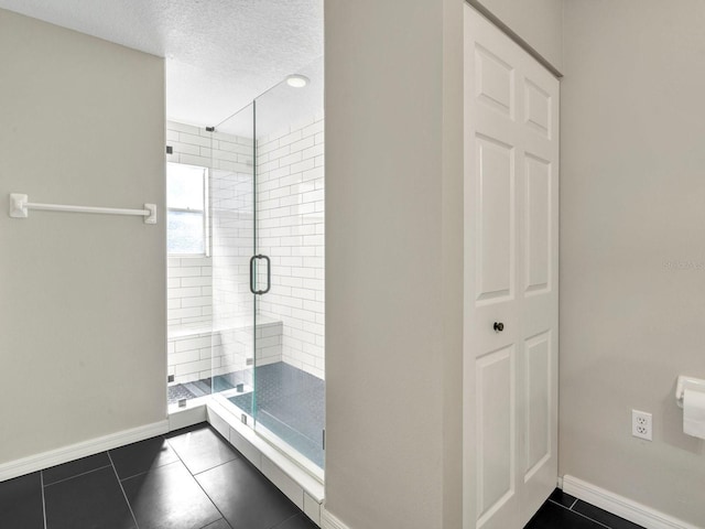 full bathroom featuring a closet, a shower stall, a textured ceiling, baseboards, and tile patterned floors