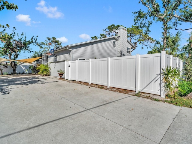 view of side of property with a garage, concrete driveway, a chimney, and fence