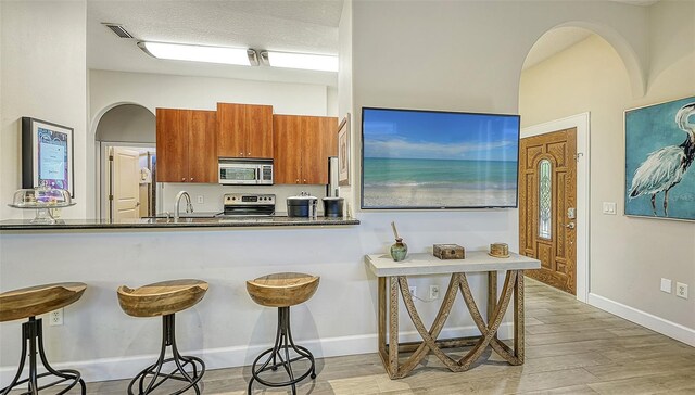 kitchen with light wood-type flooring, brown cabinets, a breakfast bar, stainless steel appliances, and arched walkways