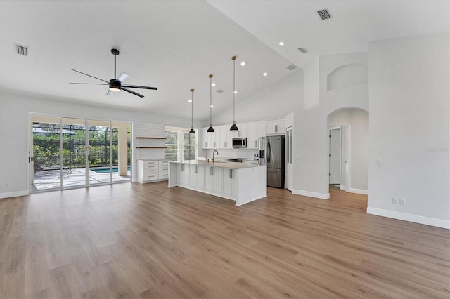 kitchen with appliances with stainless steel finishes, light hardwood / wood-style floors, white cabinets, a center island with sink, and decorative light fixtures