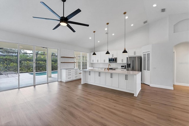 kitchen featuring pendant lighting, hardwood / wood-style floors, stainless steel appliances, white cabinets, and a center island with sink