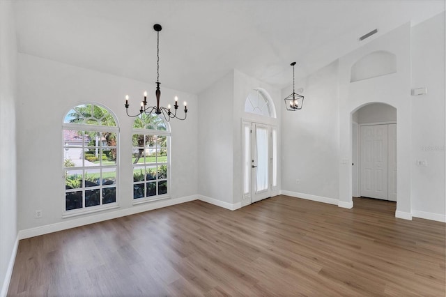 unfurnished dining area featuring wood-type flooring, high vaulted ceiling, and a chandelier