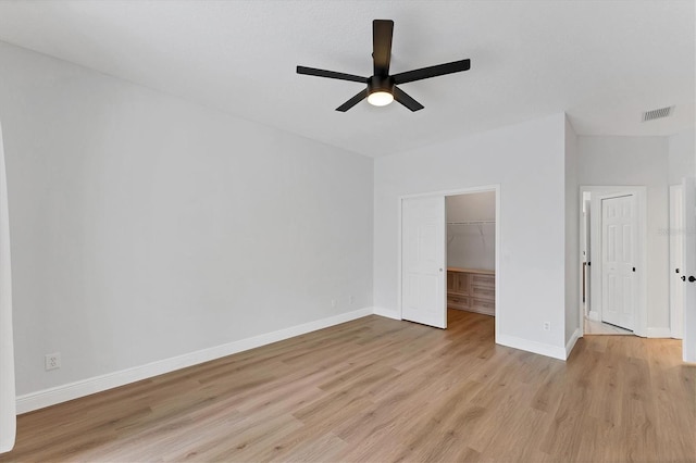 unfurnished bedroom featuring ceiling fan, a walk in closet, light wood-type flooring, and a closet