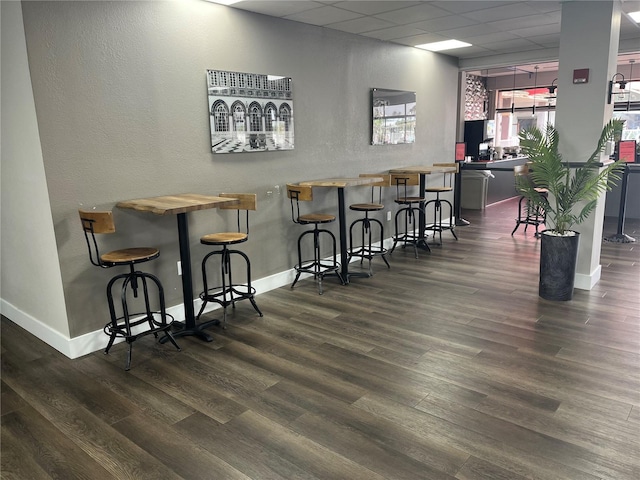 bar with a drop ceiling, dark wood finished floors, and baseboards