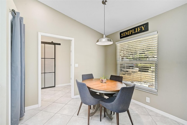 dining room with a barn door, light tile patterned flooring, and vaulted ceiling