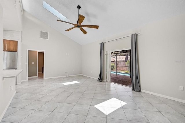 tiled empty room featuring ceiling fan, high vaulted ceiling, and a skylight