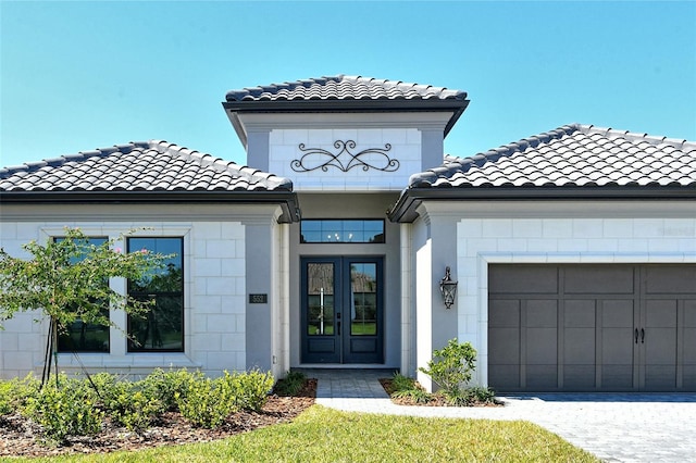 doorway to property with french doors, a tile roof, driveway, and a garage