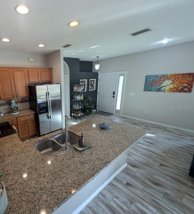 kitchen with sink, light stone counters, light hardwood / wood-style flooring, a textured ceiling, and stainless steel fridge