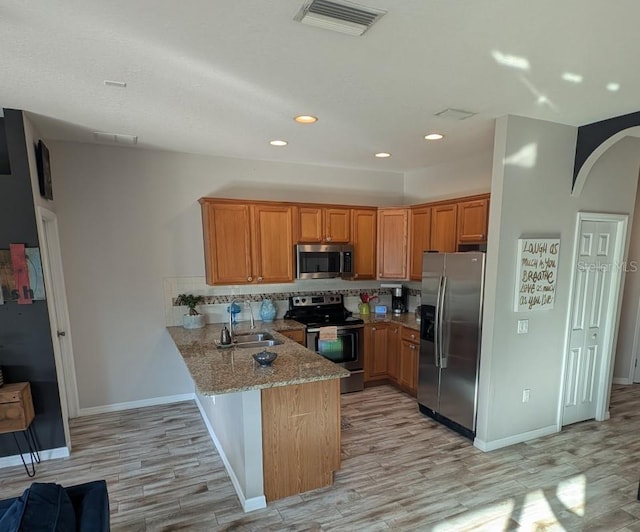 kitchen with sink, appliances with stainless steel finishes, light stone counters, kitchen peninsula, and light wood-type flooring