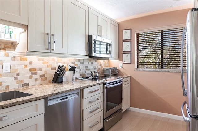 kitchen featuring appliances with stainless steel finishes, plenty of natural light, tasteful backsplash, white cabinets, and light stone countertops