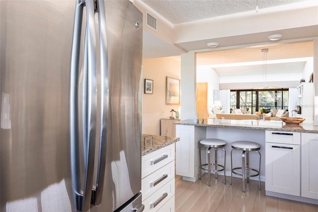 kitchen with a breakfast bar, white cabinetry, stainless steel fridge, light hardwood / wood-style floors, and light stone countertops