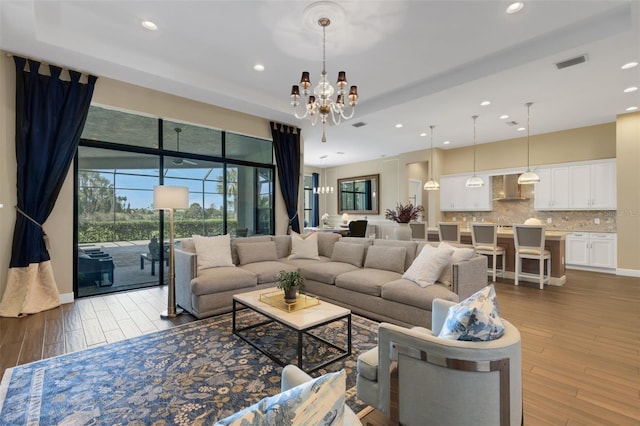 living room featuring an inviting chandelier, a tray ceiling, visible vents, and wood finished floors