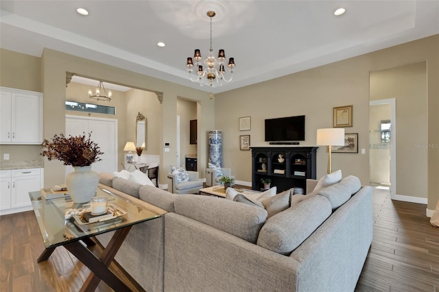 living room featuring recessed lighting, baseboards, dark wood-style floors, a tray ceiling, and an inviting chandelier