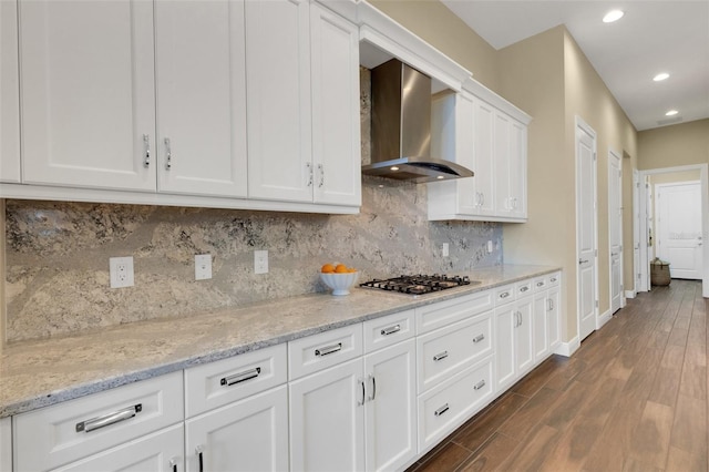 kitchen with dark wood finished floors, stainless steel gas stovetop, white cabinets, light stone countertops, and wall chimney exhaust hood